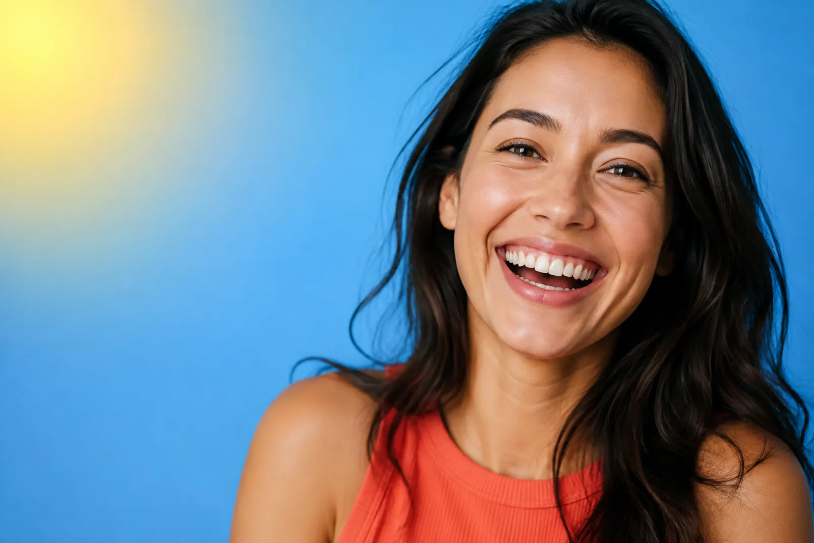 A joyful woman laughing and showing her natural smile against a bright blue background