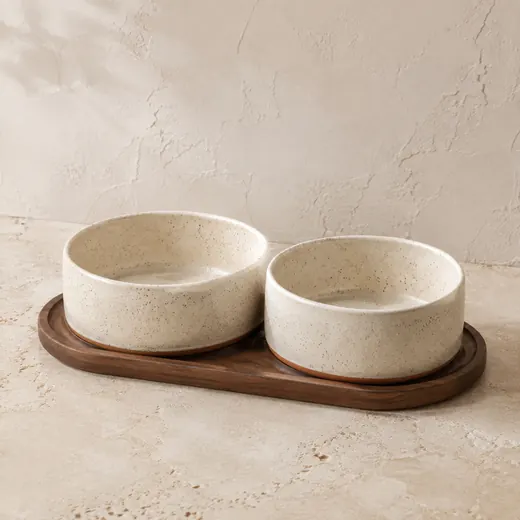 Two speckled cream stoneware pet bowls on a walnut tray